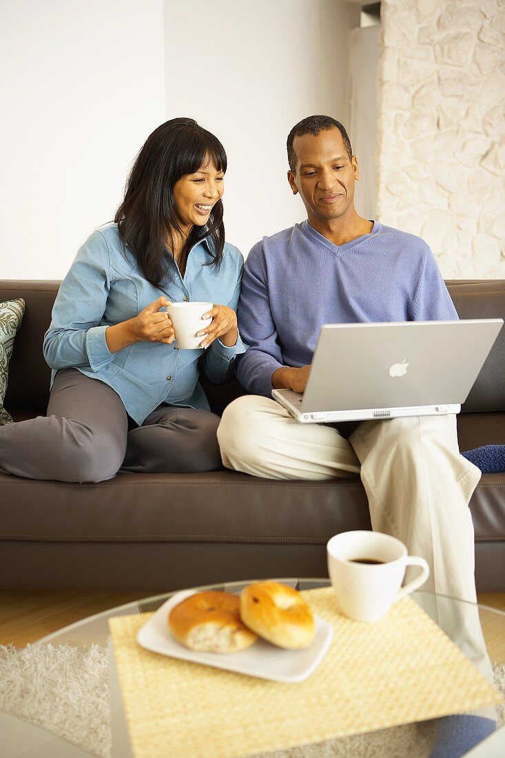 Frau mit Kaffeetasse neben Mann mit Computer auf dem Sofa