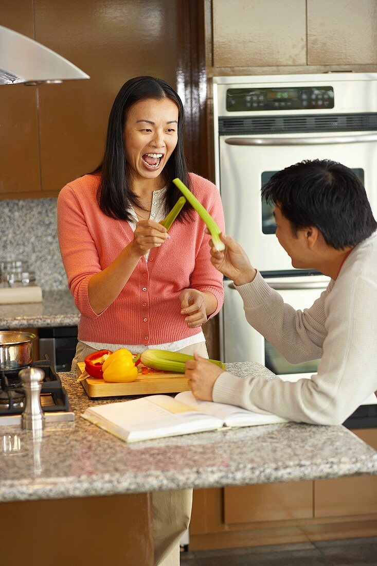 Young couple larking about with celery in kitchen