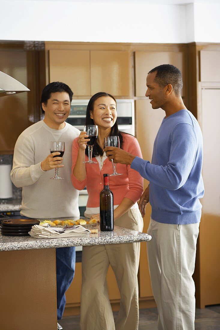 Three people drinking red wine in kitchen