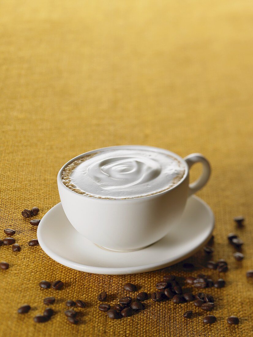 Tasse Cappuccino, umgeben von Kaffeebohnen