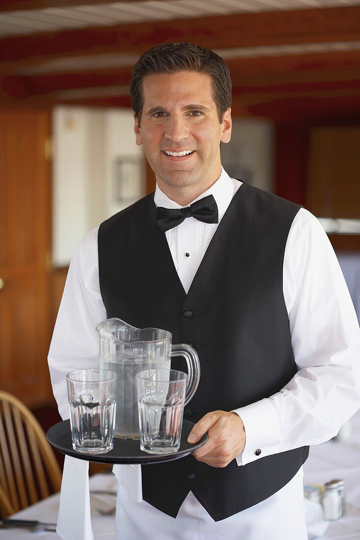 Kellner serviert Wasserkrug und Gläser im Restaurant