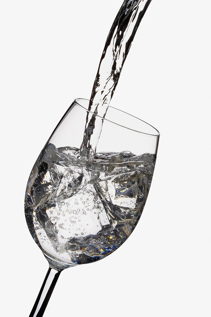 Wasser in Glas mit Eiswürfeln einschenken