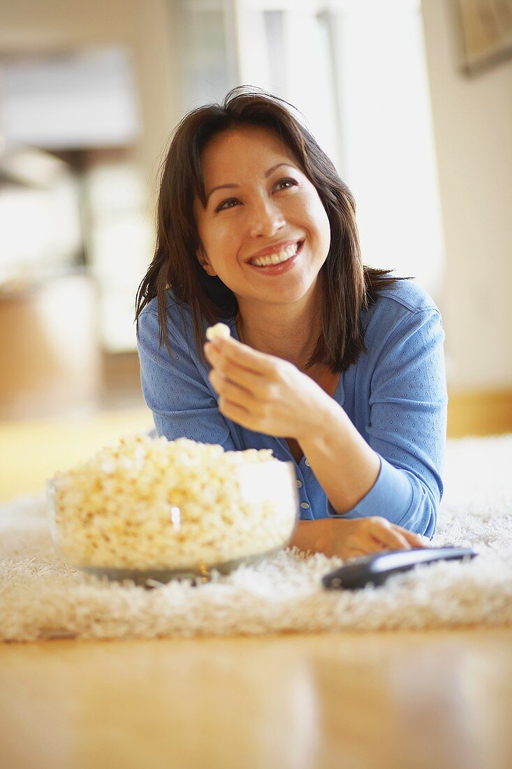 Frau isst Popcorn, auf dem Teppich liegend