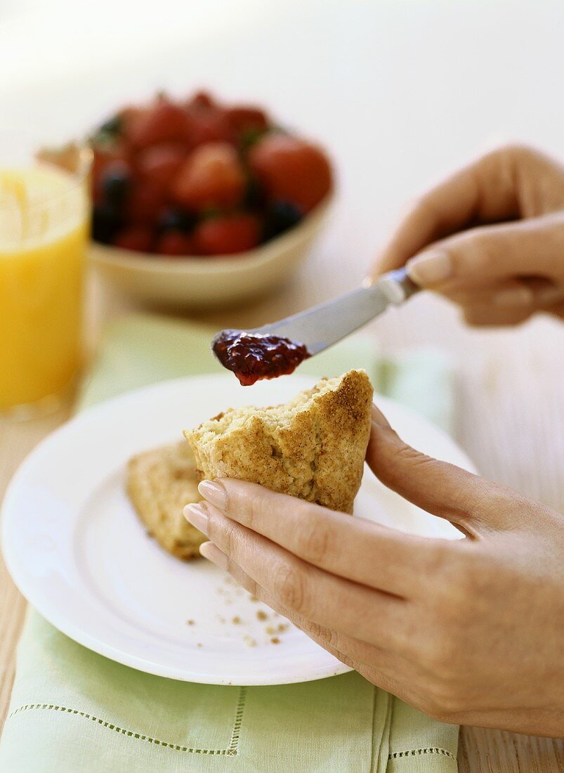 Hands Holding a Cinnamon Scone and a Knife with Strawberry Jam