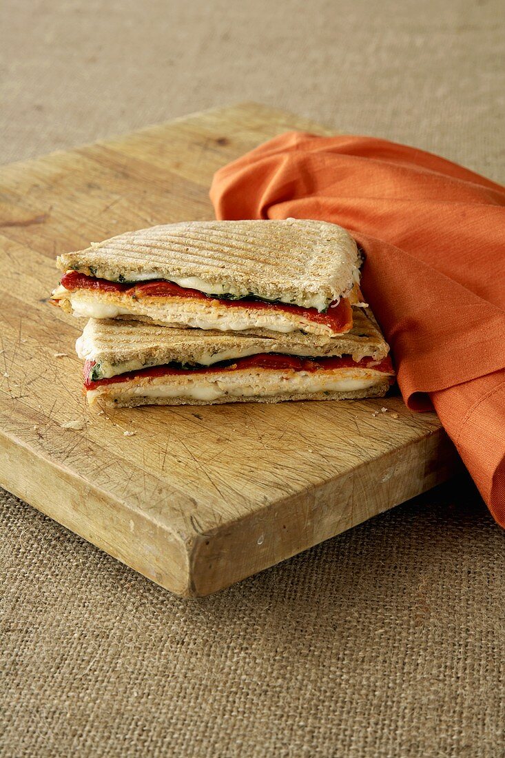 A Chicken Panini on a Wooden Board with an Orange Napkin