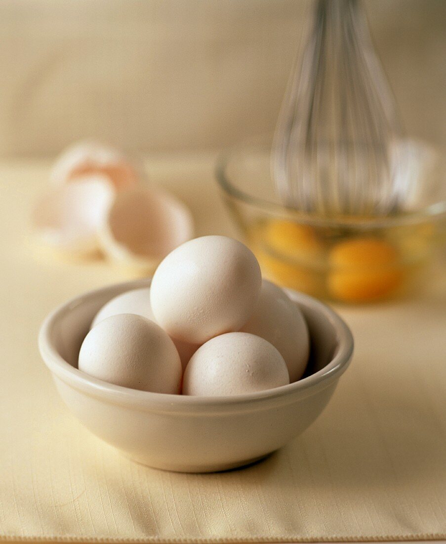 Eier in einer Schale, im Hintergrund aufgeschlagene Eier