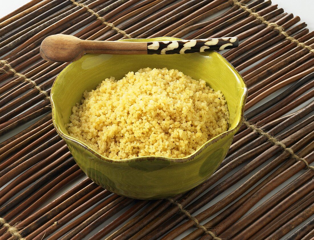 Couscous Served in a Green Bowl with Wooden Spoon on Bamboo Mat