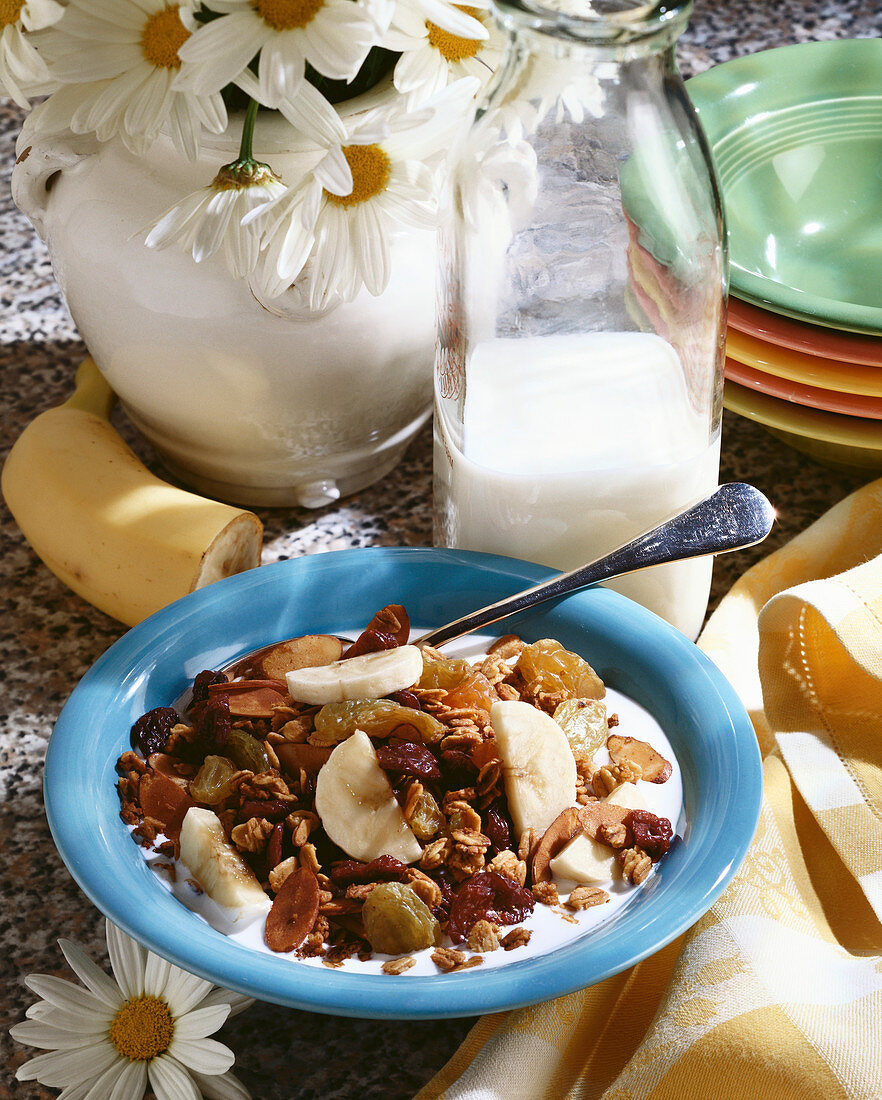 Bowl of Granola Cereal with Dried Fruit and Banana Slices; Milk and Flowers