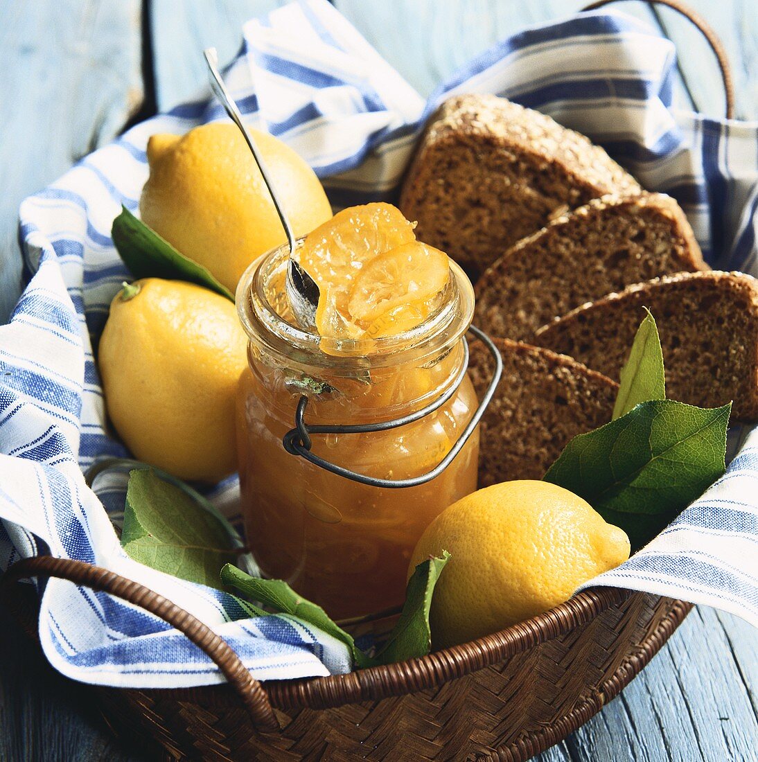 Glas Zitronenmarmelade, frische Zitronen und Brot im Korb