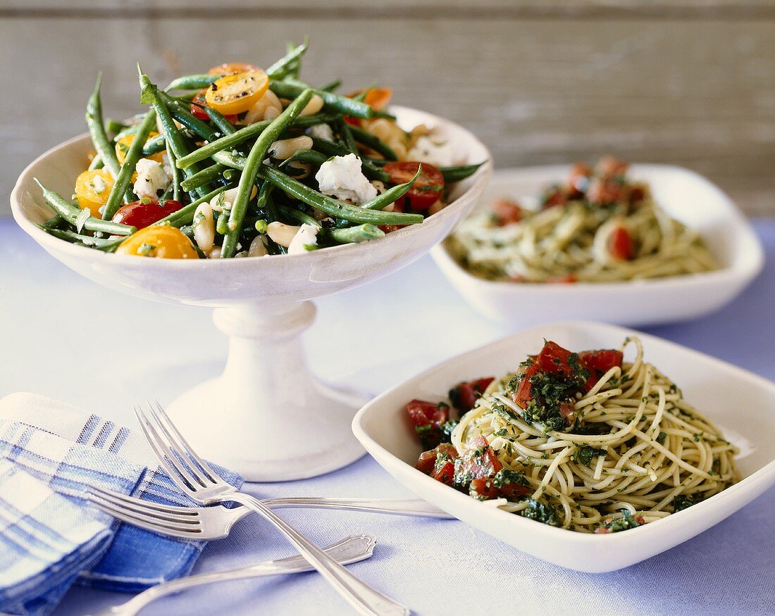 Spaghetti with Tomatoes and Pesto in Bowls with Green Bean and Tomato Salad in Serving Bowl