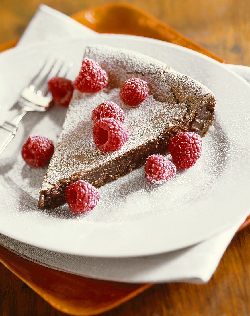 Slice of Chocolate Tart with Raspberries and Powdered Sugar on a Plate