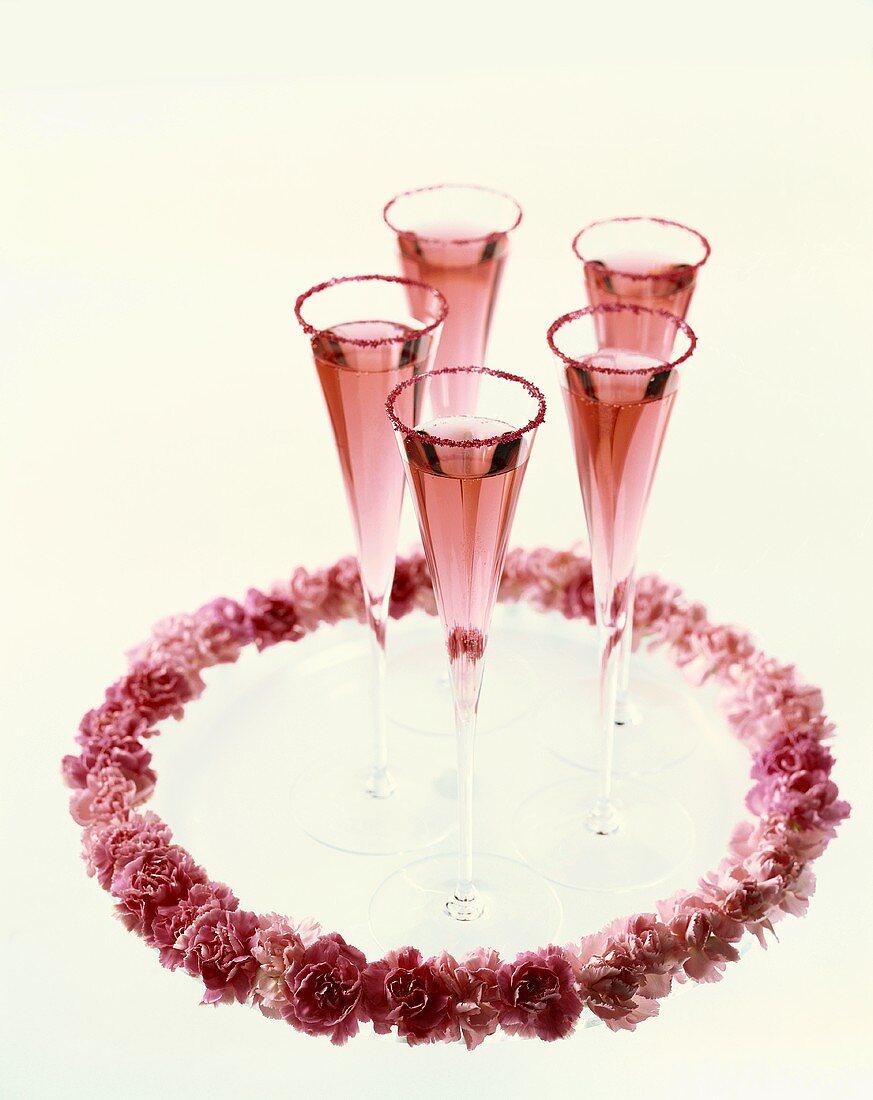 Rosé-Champagner in Champagnerflöten und rosa Blumenkranz