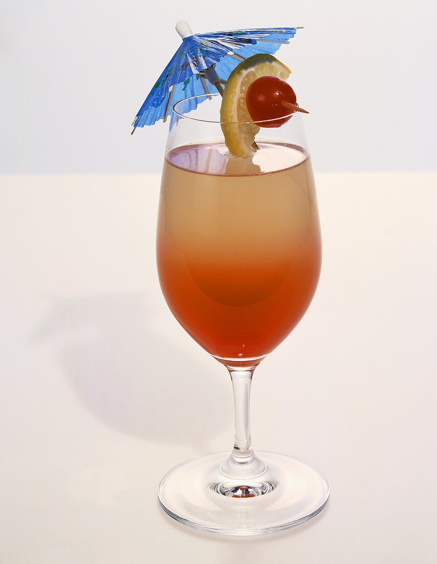 Cocktail in a Stem Glass with Blue Cocktail Umbrella and Lime and Cherry Garnish on White Background