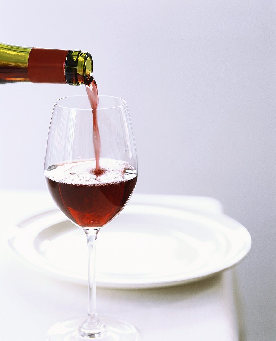 Rotwein aus Flasche in Glas gießen