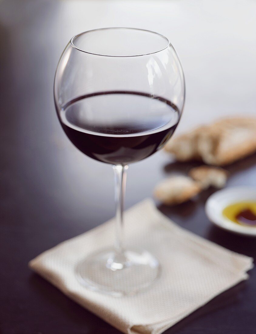 Glas Rotwein auf weisser Serviette, Weißbrot, Olivenöl