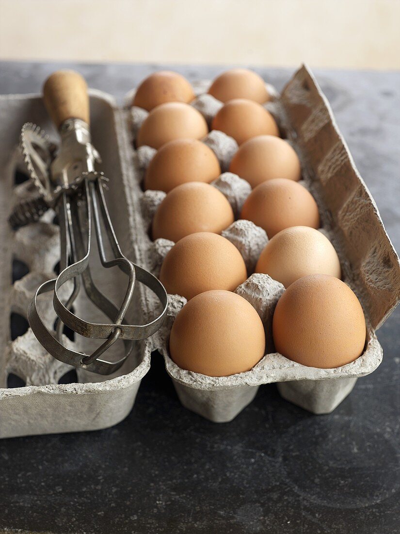 A Dozen Brown Eggs in an Opened Carton with Handheld Beaters