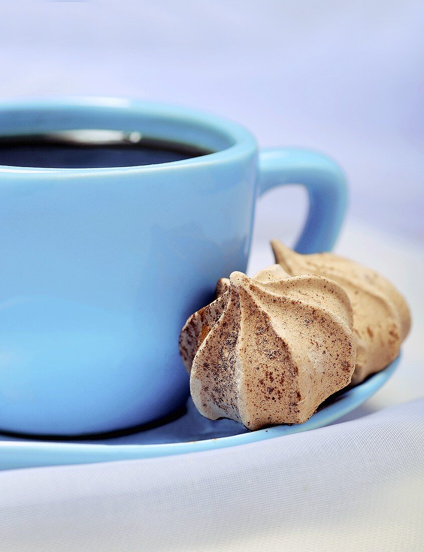 Schwarzer Kaffee in blauer Tasse mit zwei Baiserplätzchen