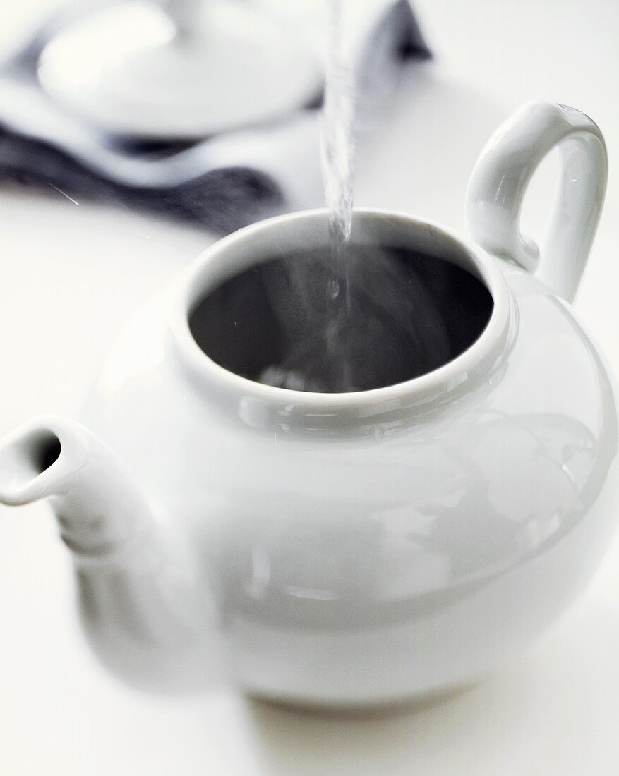 Kochendes Wasser in weiße Teekanne gießen