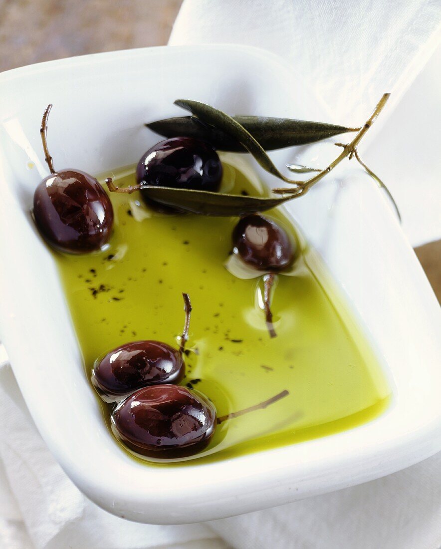 Schwarze Oliven mit Blättern in Olivenöl