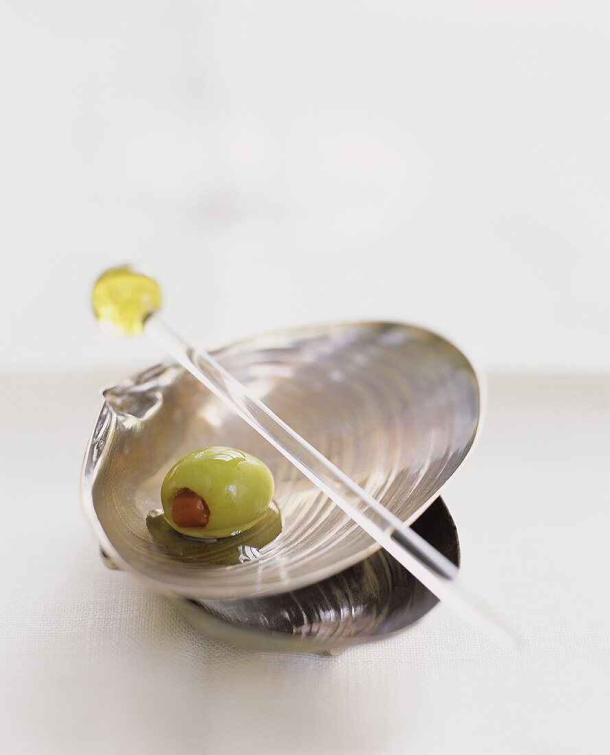 Gefüllte Olive in Muschelschale und Cocktailstäbchen