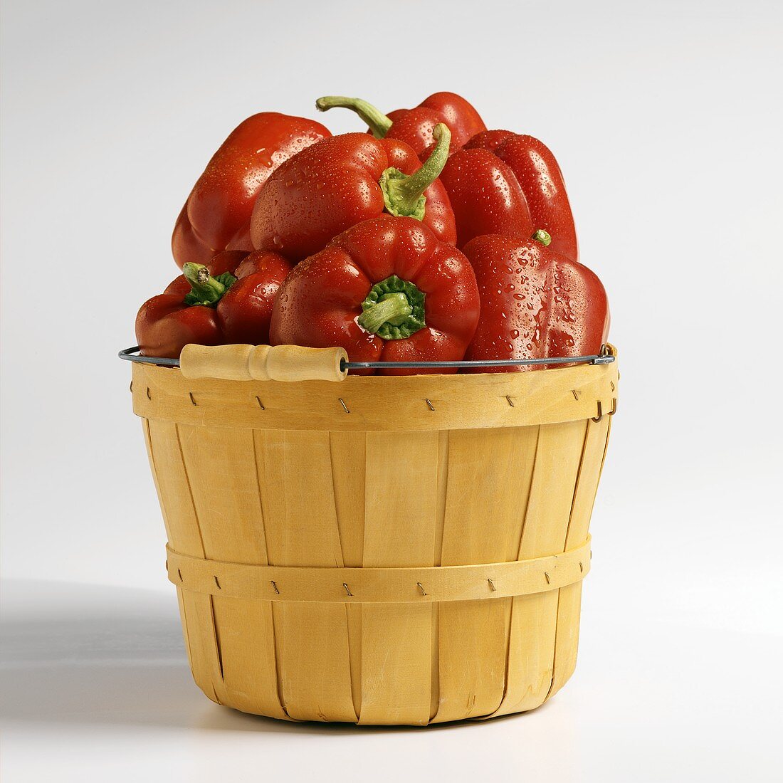 Wooden Market Basket Filled with Red Bell Peppers with Dew on White Background