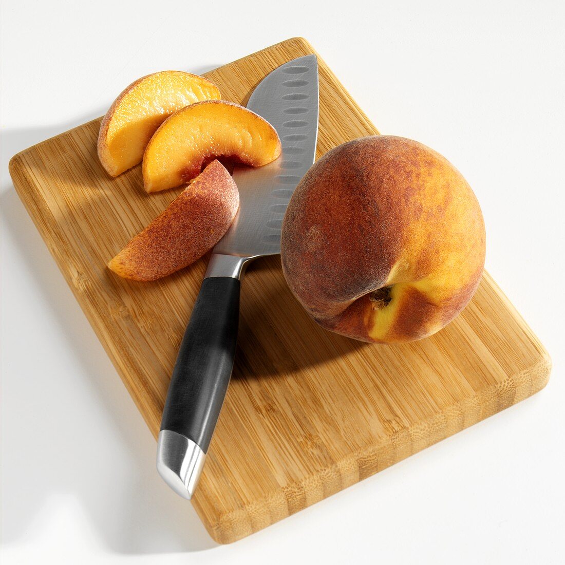 Whole peach and peach slices on wooden board with knife