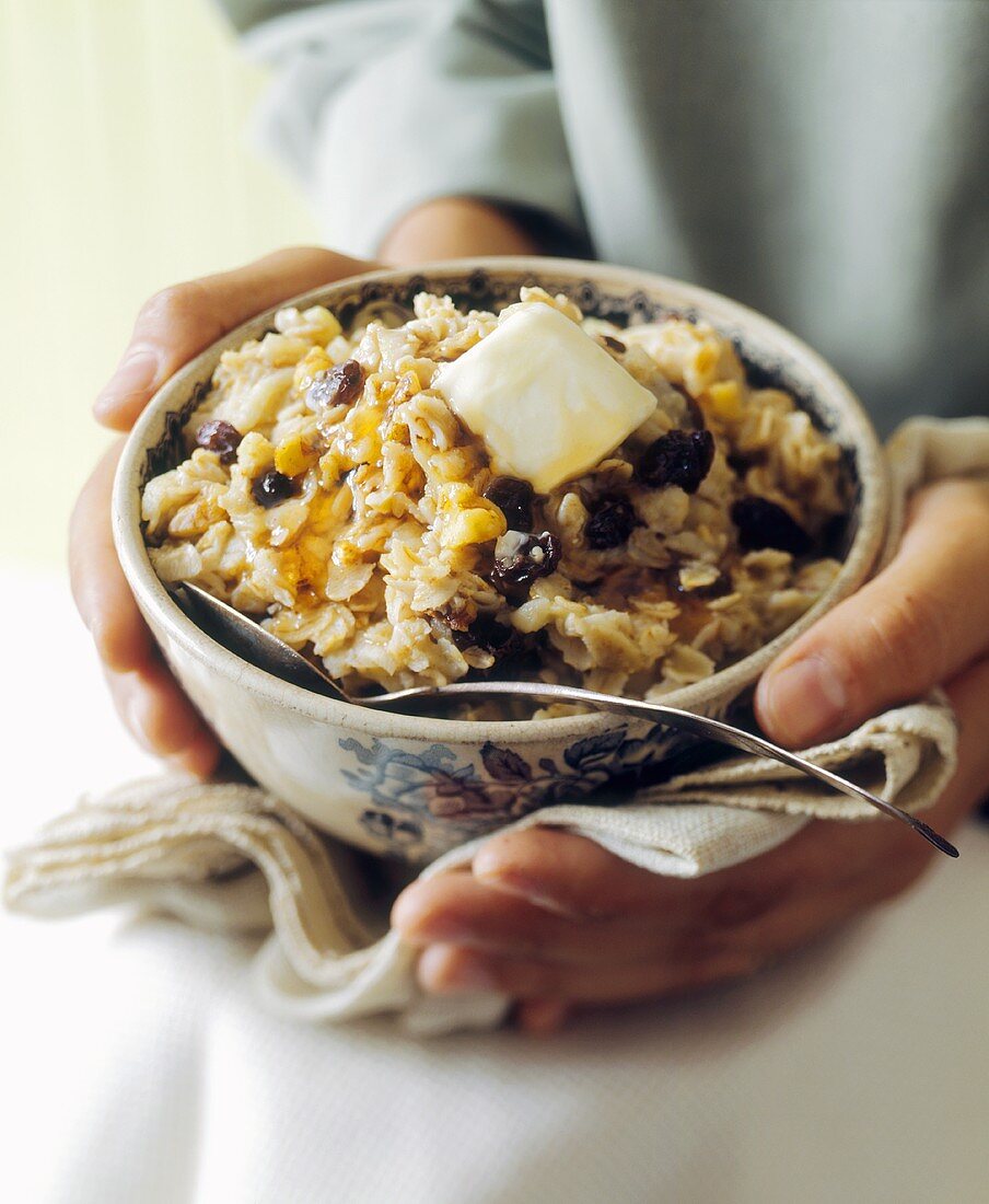 Hands holding bowl of oat flakes with butter and syrup