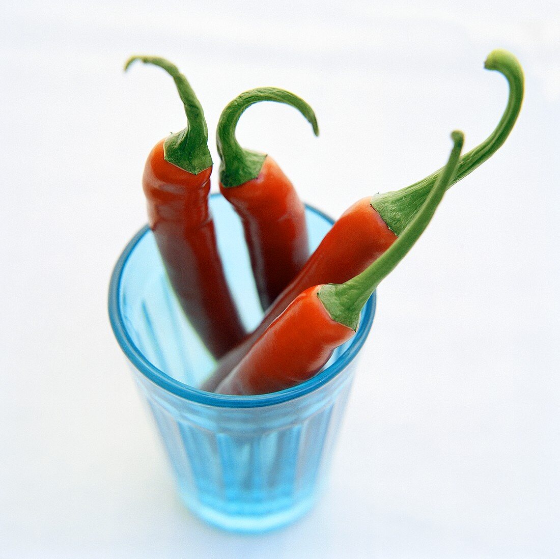 Four Whole Red Chili Peppers with Stems in a Blue Glass