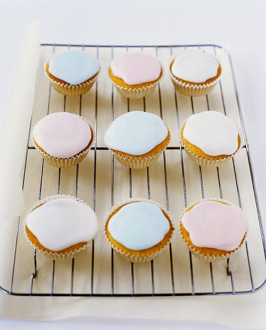 White Cup Cakes with Pastel Blue, Pink and White Icing on Cooling Rack