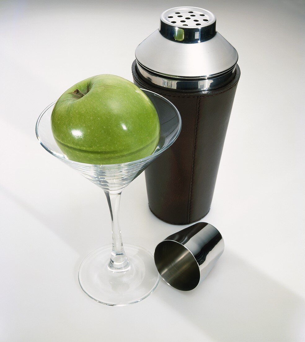 Ein Granny Smith im Martiniglas, dahinter Cocktailshaker