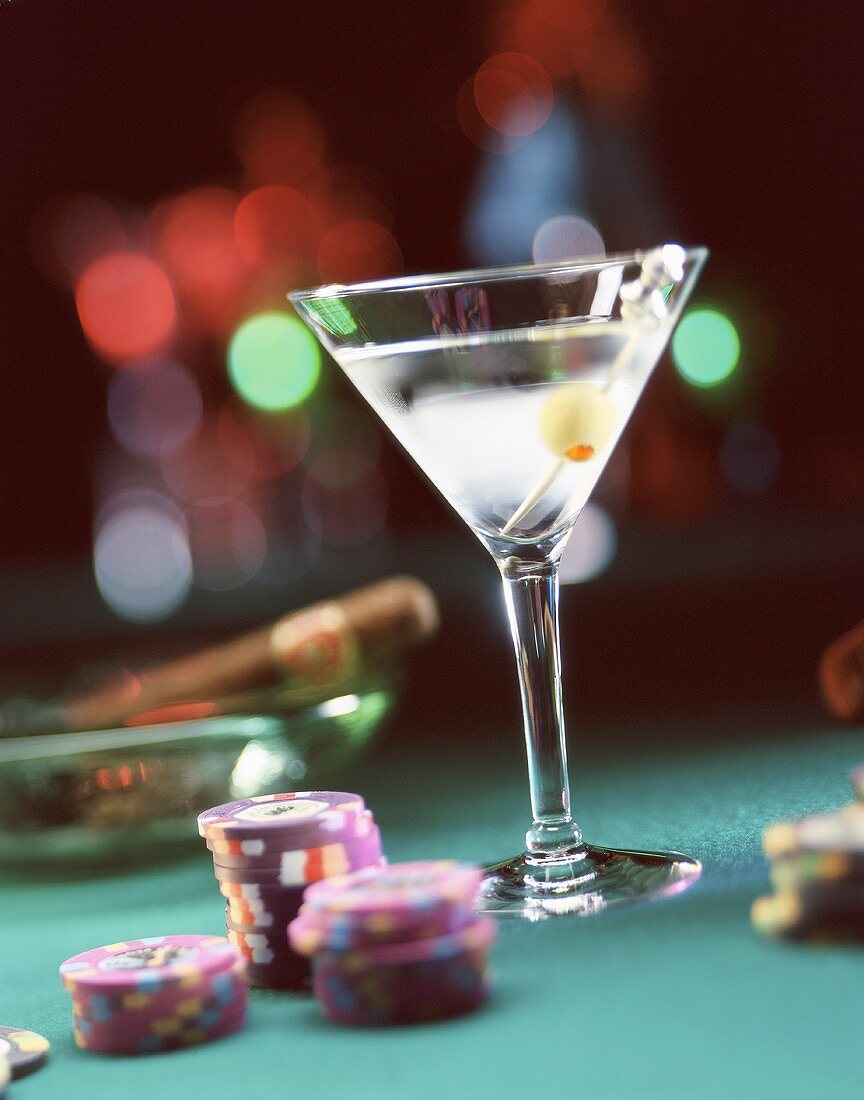 A Martini glass, casino chips and a cigar on an ashtray in the background