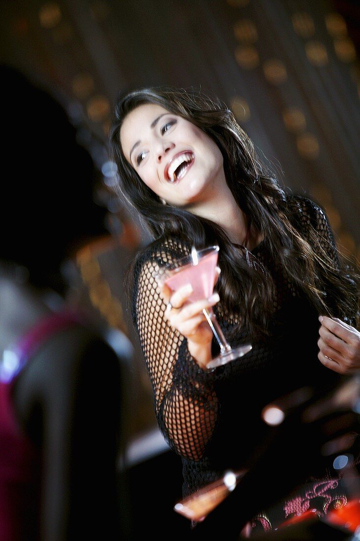 Lachende Frau mit Cocktail im Nachtclub