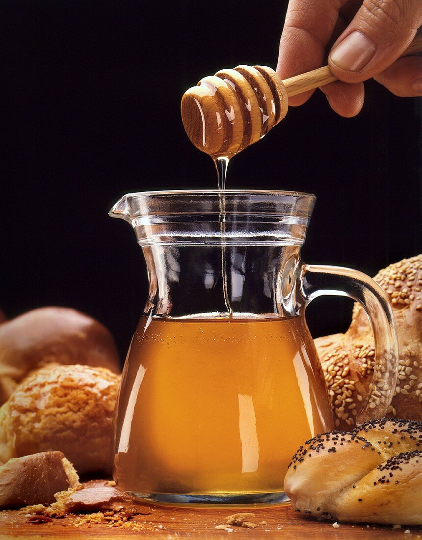 Honey flowing from a honey spoon into a glass jug