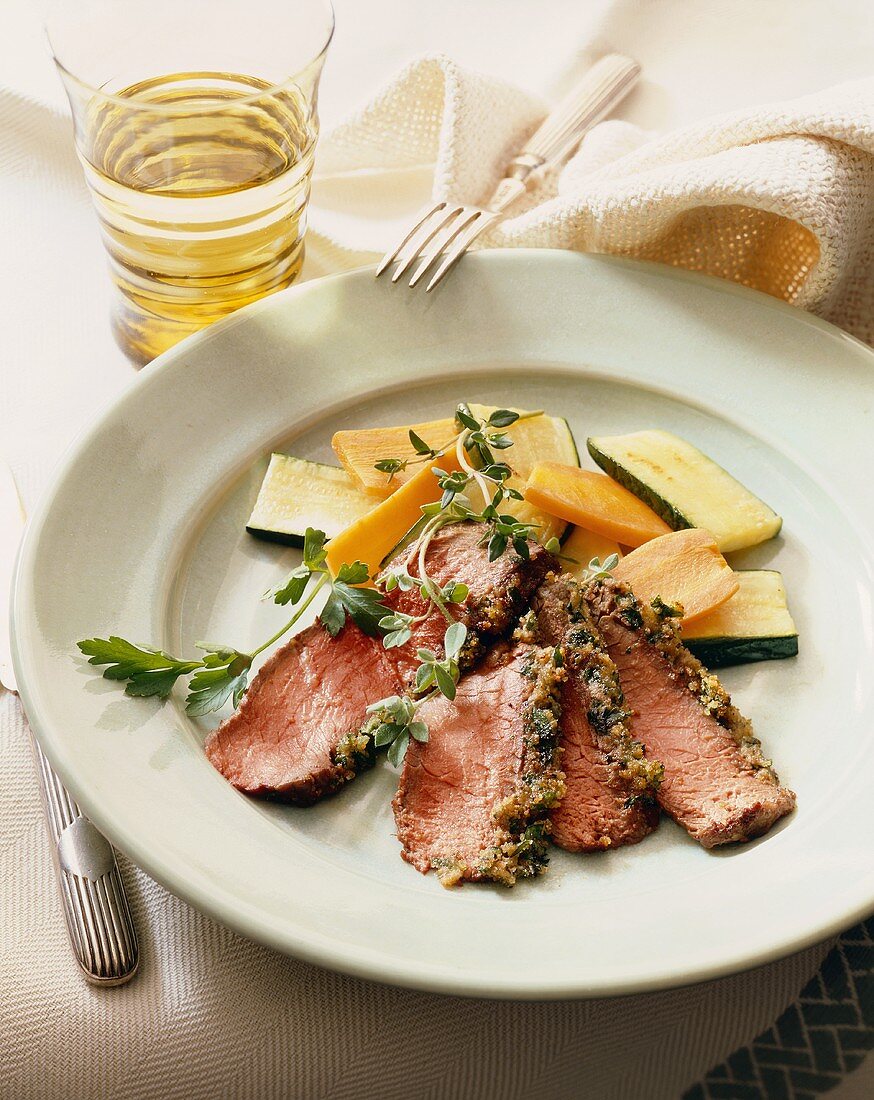 Sliced Herb Crusted Steak Cooked Rare on a Plate with Sliced Vegetables; Fork and Knife