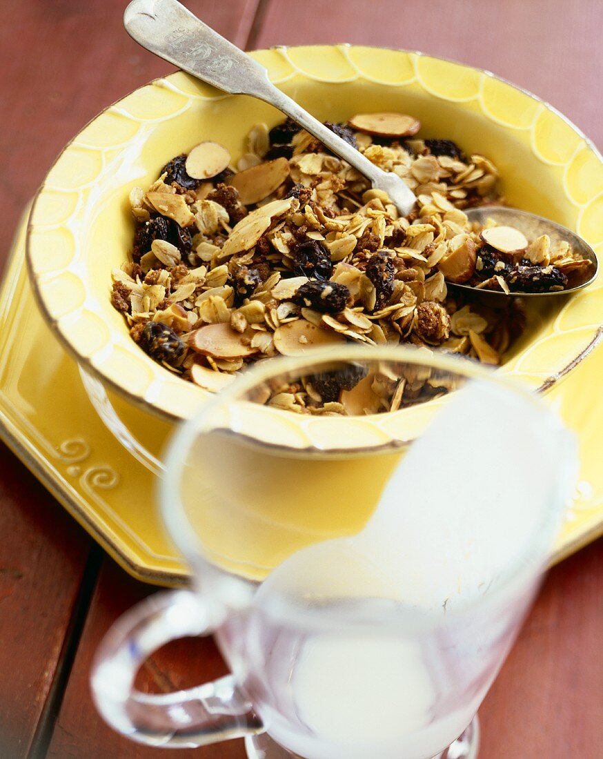 Granola with Raisins in a Yellow Bowl with Spoon; Empty Milk Pitcher