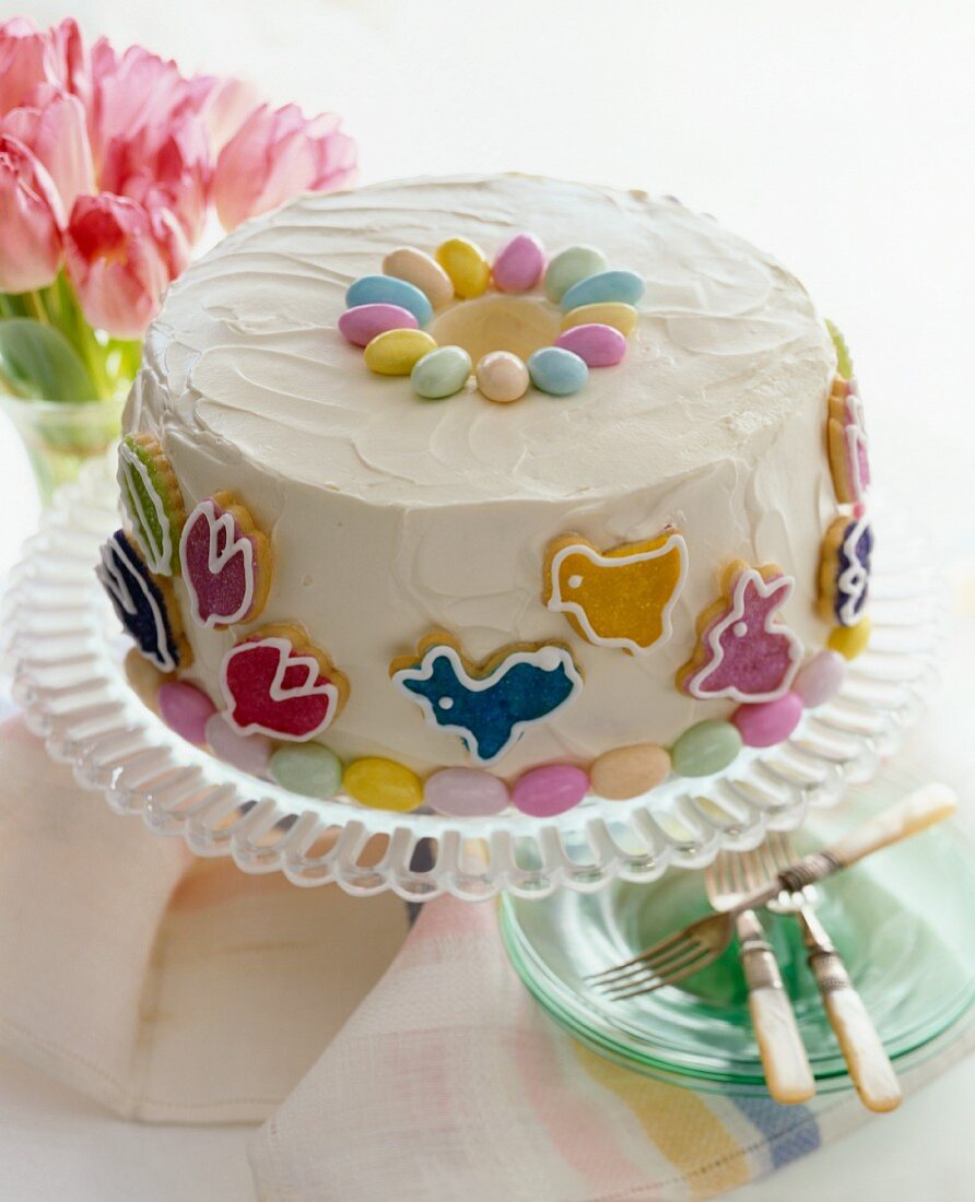 Easter Cake Decorated with Easter Candies on a Cake Plate; Stack of Plates with Forks