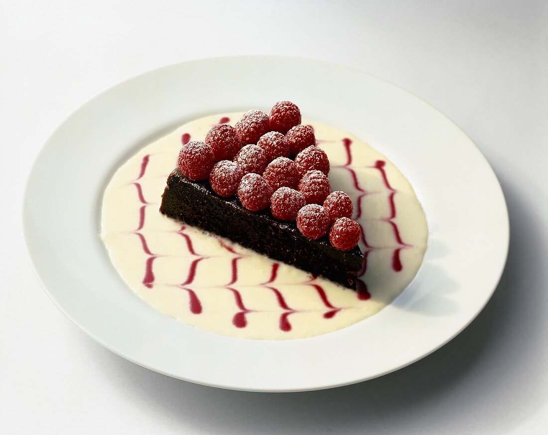 Slice of Chocolate Tart Topped with Fresh Raspberries in a Decorative Sauce on White Plate