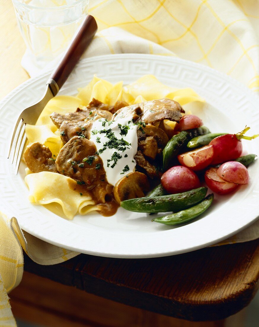 Beef Stew Over Egg Noodles with Sour Cream; Snap Peas and Red Potatoes on a Plate with Fork