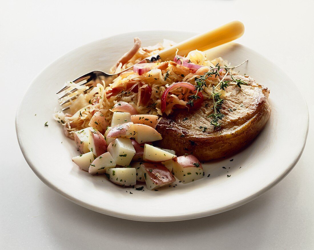 Schweinekotelett mit Sauerkraut & roten Kartoffeln auf Teller