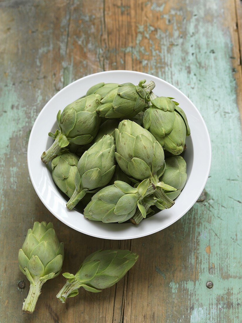 Small Artichokes in and Beside a Bowl of Rustic Wooden Table