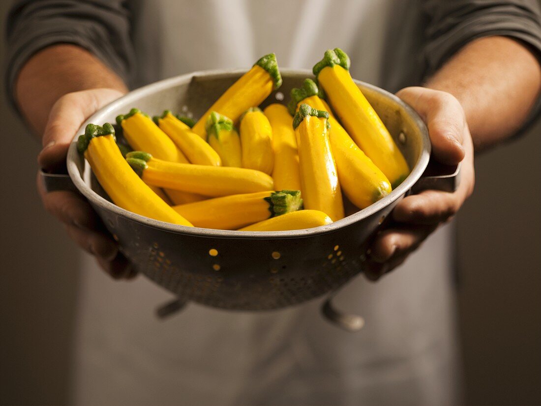 Mann hält Küchensieb mit gelben Zucchini
