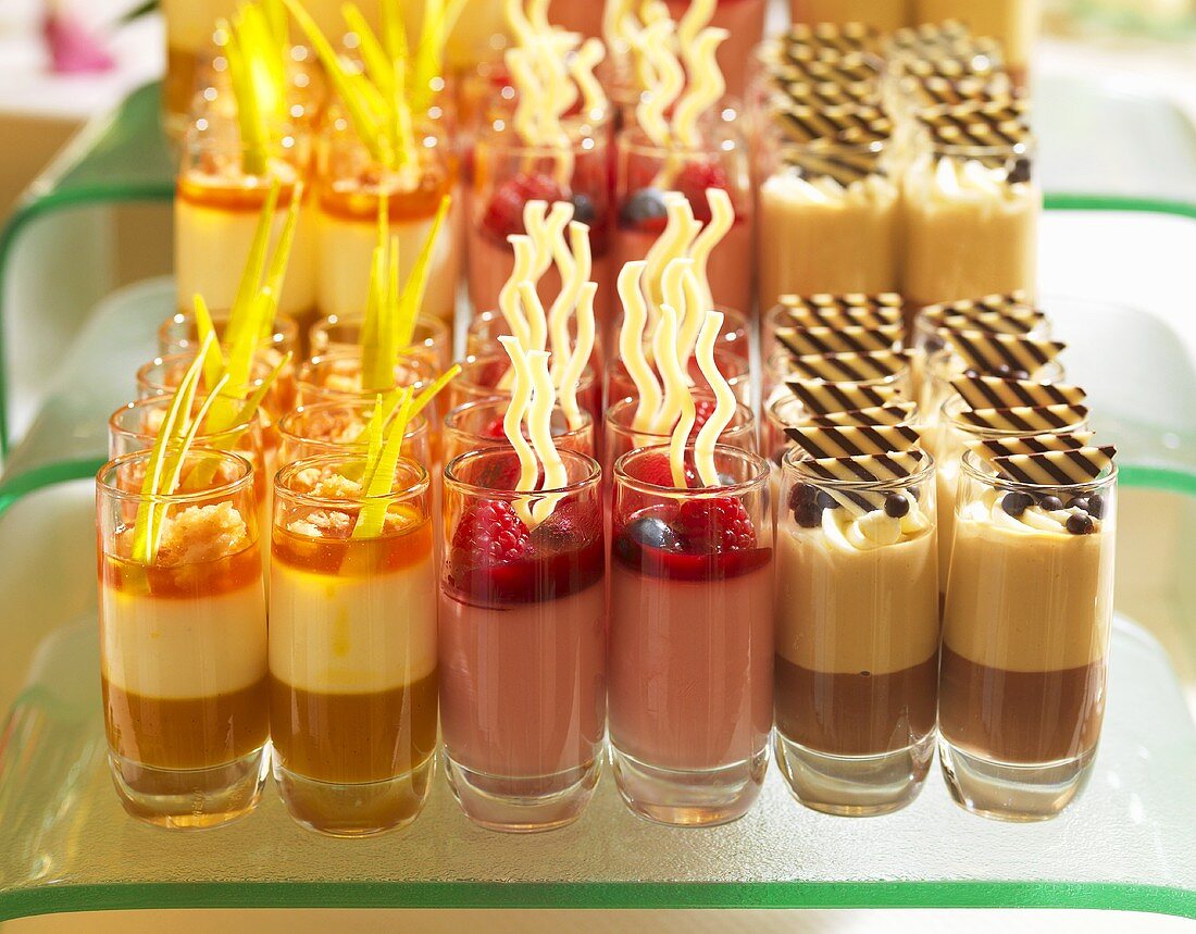 Verschiedene cremige Desserts in Reihen von Gläsern