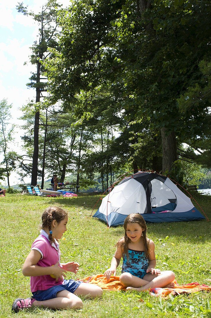 Zwei Mädchen auf der Wiese, im Hintergrund Campingzelt