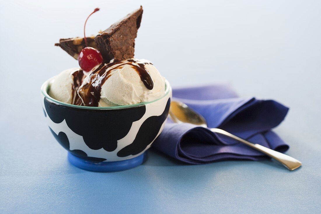 Ice Cream Sundae in a White and Black Bowl; Blue Napkin and Spoon