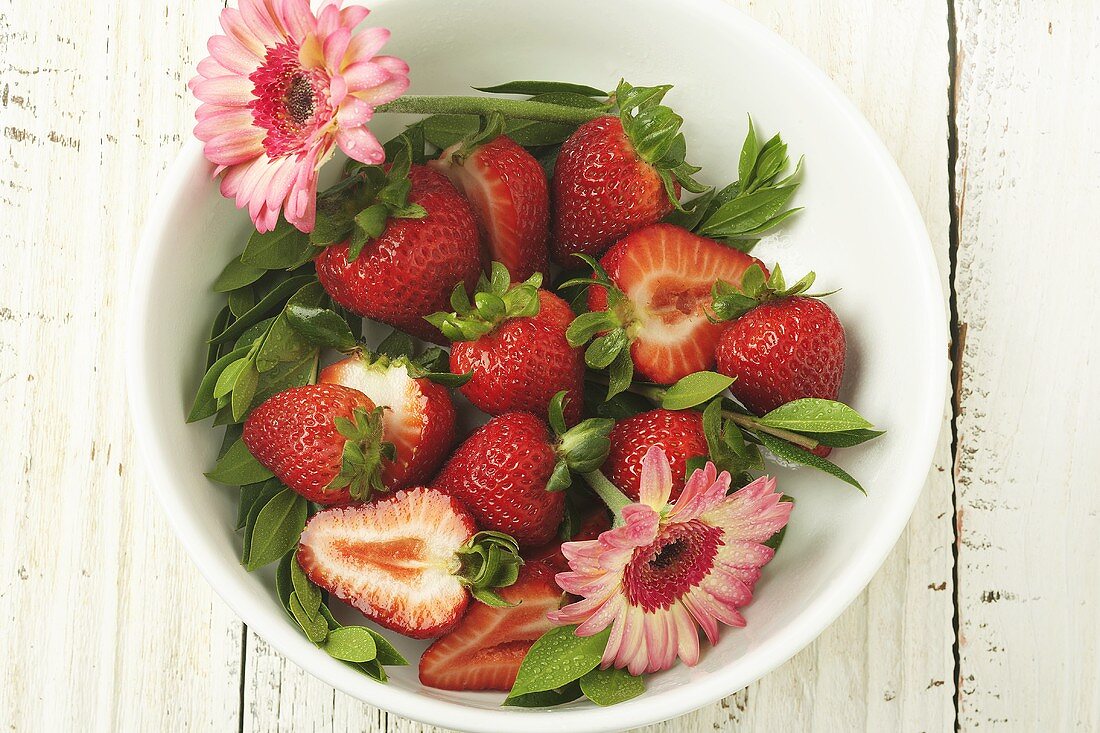 Whole and Sliced Fresh Strawberries in a Bowl; Pink Flowers