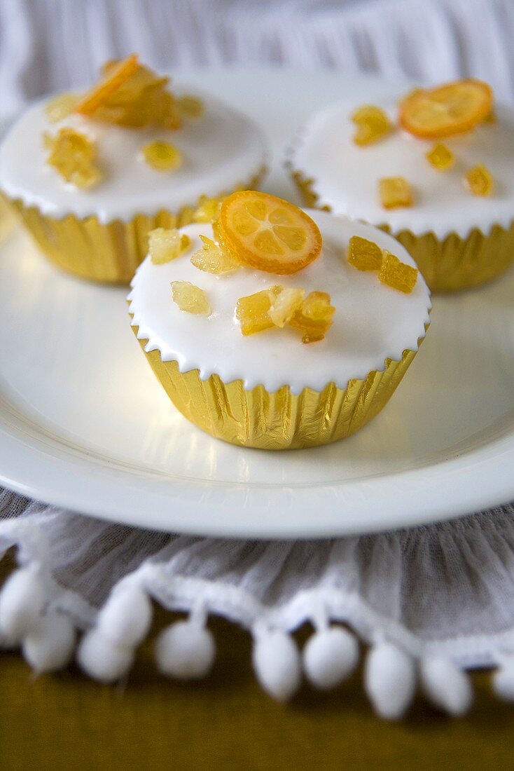 Mehrere Cupcakes mit Zuckerglasur und Kumquats