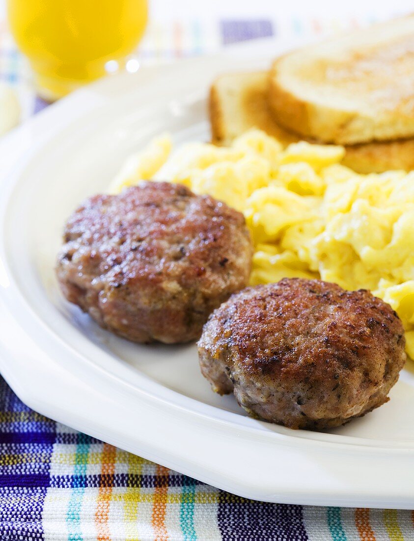 Breakfast Sausage Patties on a Plate with Scrambled Eggs and Toast; Orange Juice