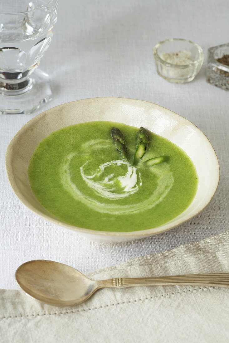 Bowl of Creamy Pea Soup with Cream Swirl and Asparagus Tips
