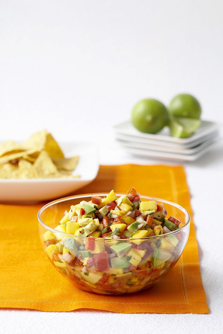 Mangosalsa in Glasschale, Tortillachips, Limetten