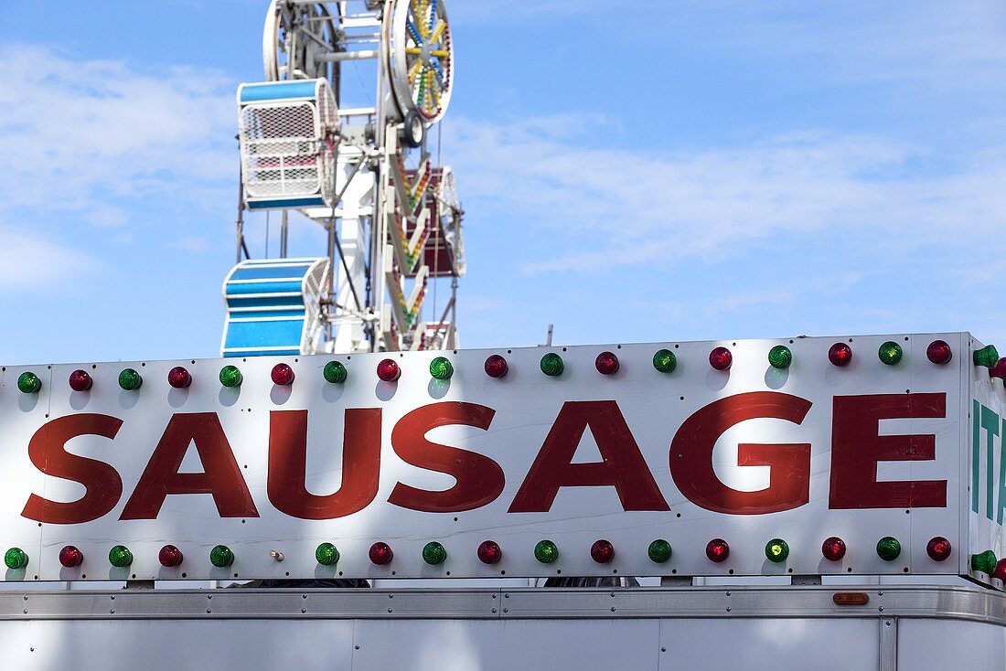 Sign for Sausage with Ferries Wheel in Background; At the Fair